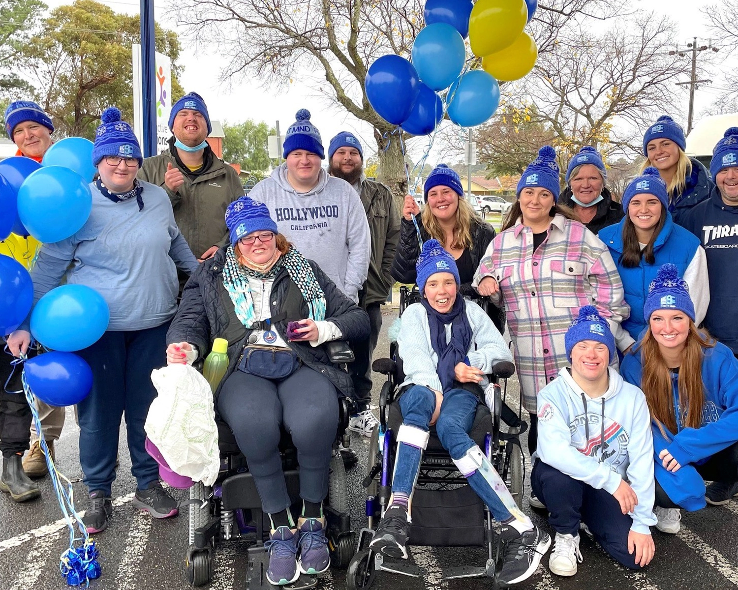 A group of people wear blue beanies and hold balloons with NDIS registered disability service Distinctive Options