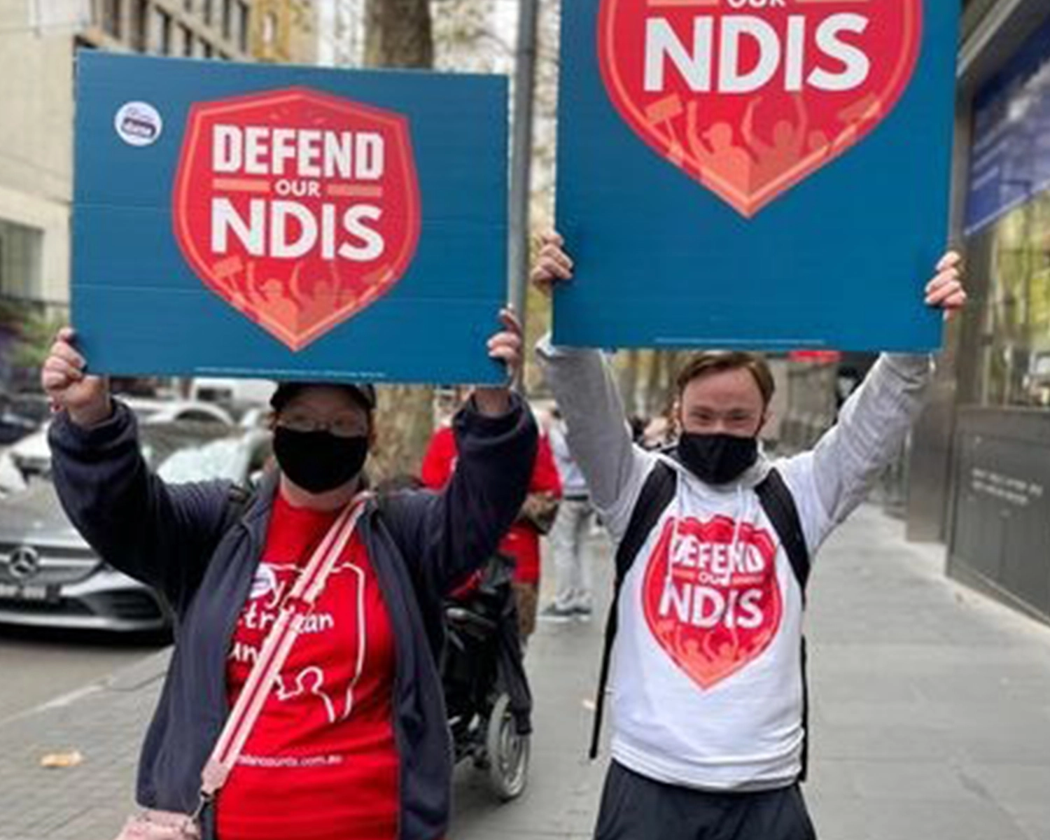 Two people hold up banners at a rally at NDIS registered disability service Distinctive Options