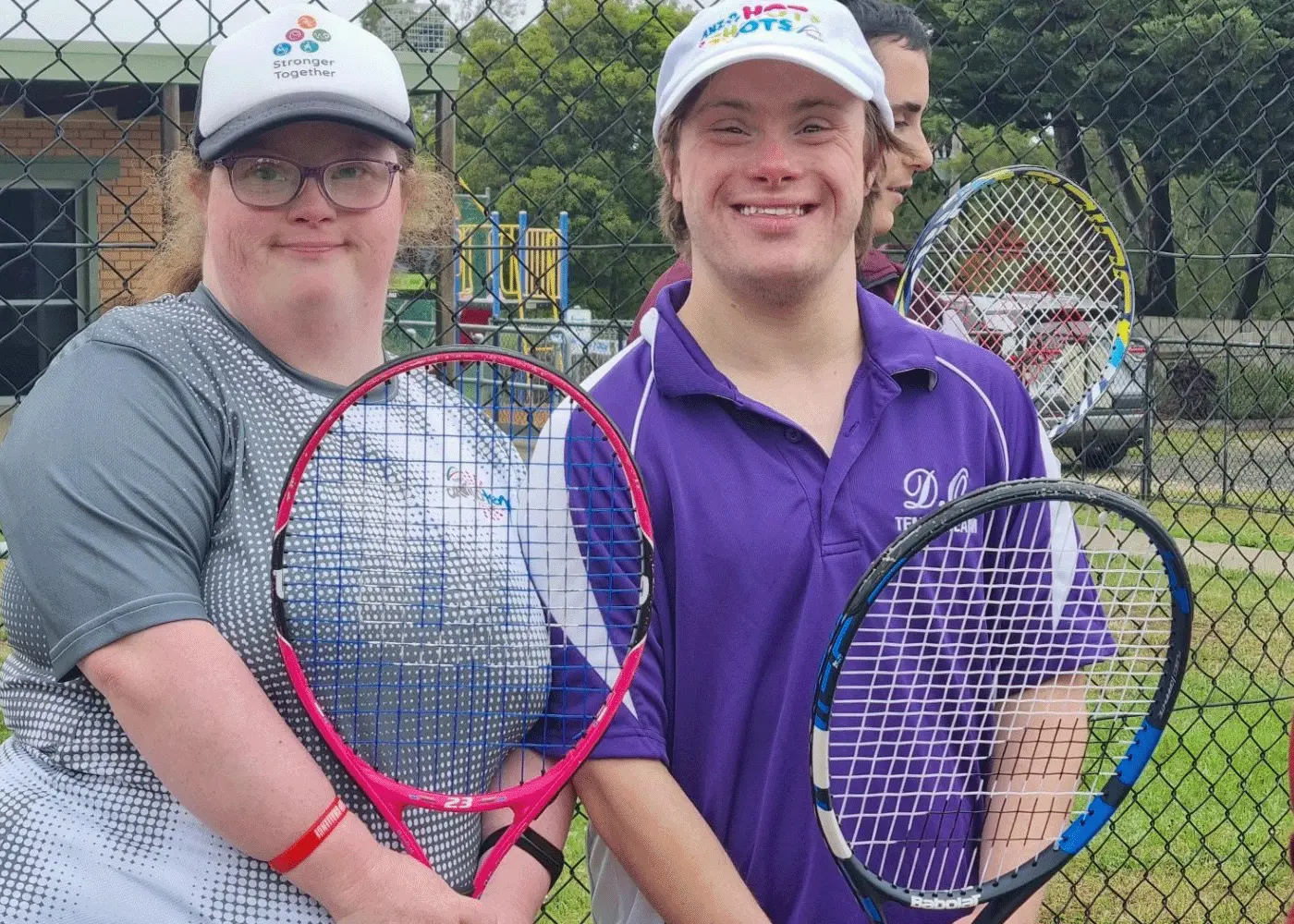 Two people hold tennis racquets while standing on a tennis court.